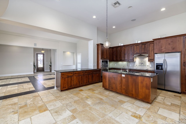 kitchen with decorative light fixtures, an island with sink, sink, backsplash, and stainless steel appliances