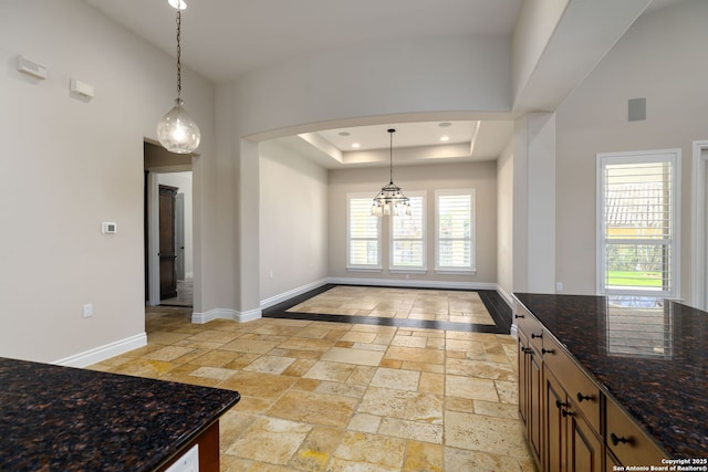 kitchen featuring a tray ceiling, decorative light fixtures, and dark stone counters