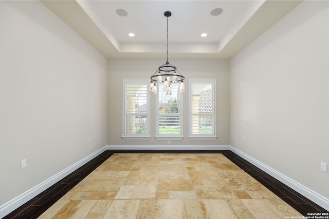 unfurnished dining area featuring hardwood / wood-style flooring, a raised ceiling, and a notable chandelier