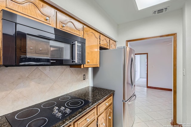 kitchen with tasteful backsplash, light tile patterned flooring, dark stone counters, and black appliances