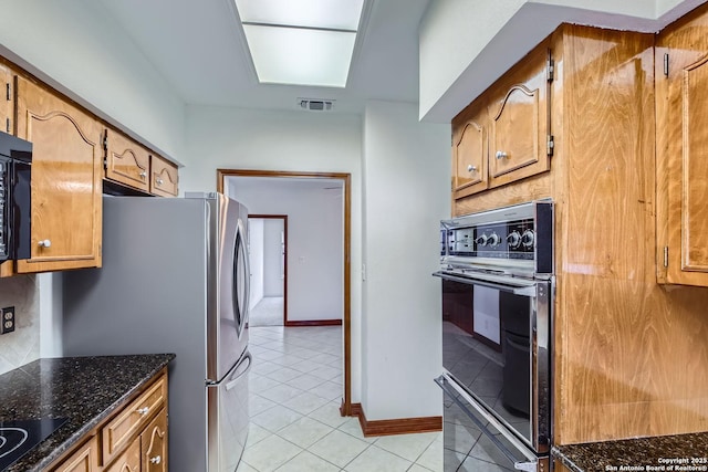 kitchen featuring double wall oven, stainless steel fridge, light tile patterned floors, and dark stone countertops