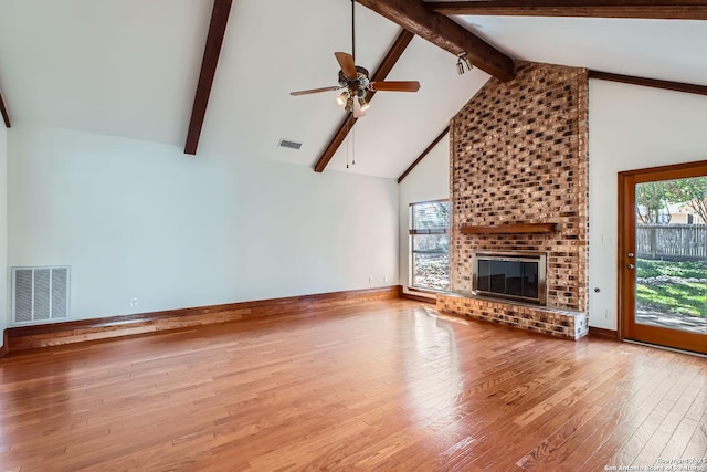 unfurnished living room with high vaulted ceiling, beamed ceiling, ceiling fan, a brick fireplace, and light hardwood / wood-style flooring