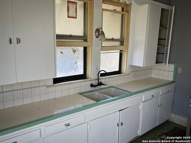 kitchen with tasteful backsplash, sink, tile counters, and white cabinets