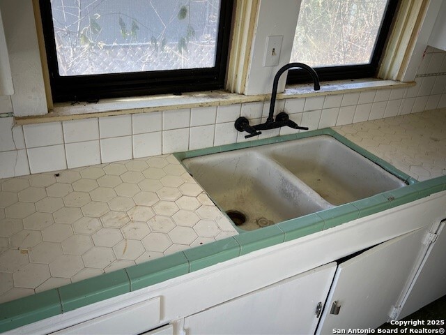 interior details with white cabinetry, sink, and tile countertops