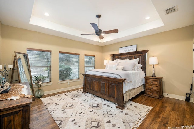 bedroom featuring a tray ceiling, dark wood-style flooring, visible vents, and baseboards