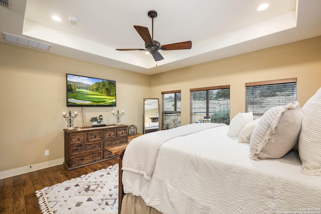 bedroom featuring a tray ceiling, dark wood-style flooring, visible vents, and baseboards