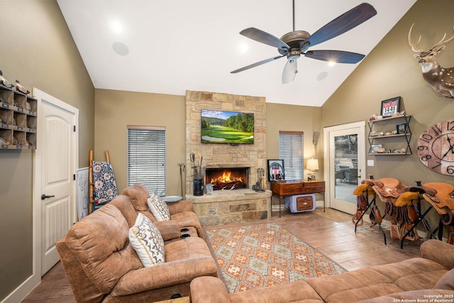 living area with ceiling fan, high vaulted ceiling, a stone fireplace, and wood finished floors