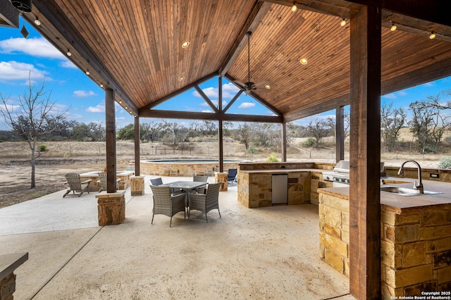 view of patio / terrace with a ceiling fan, outdoor dining space, a sink, exterior kitchen, and a rural view