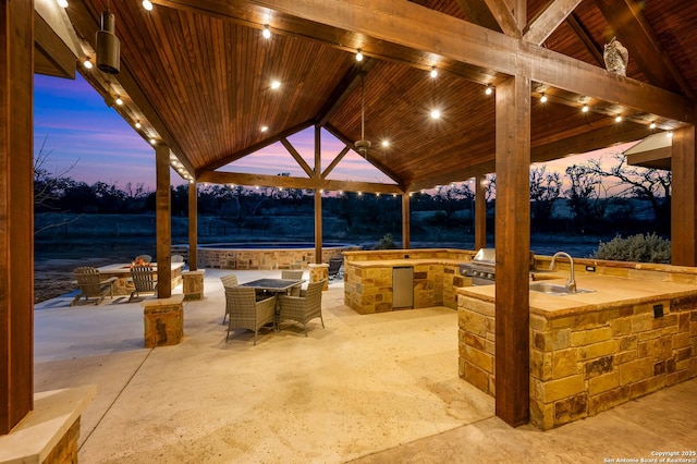 patio terrace at dusk featuring outdoor dining space, a gazebo, a sink, and area for grilling