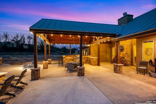 patio terrace at dusk featuring a sink, an outdoor kitchen, an outdoor bar, and a gazebo