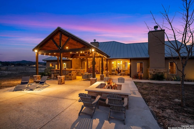 back of property featuring a chimney, a standing seam roof, a patio area, metal roof, and a fire pit