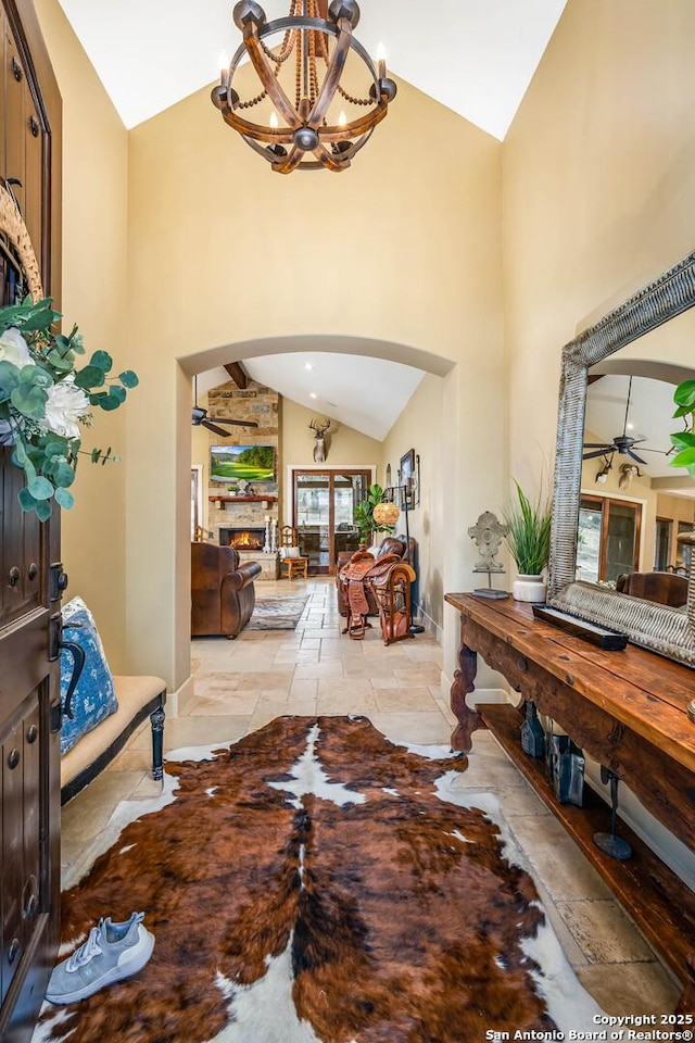 foyer featuring arched walkways, stone tile flooring, a fireplace, high vaulted ceiling, and ceiling fan with notable chandelier