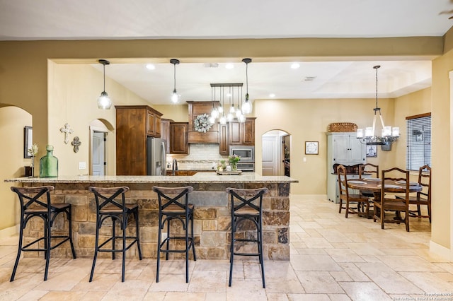 kitchen featuring arched walkways, light stone counters, a breakfast bar area, appliances with stainless steel finishes, and pendant lighting