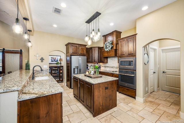 kitchen featuring a barn door, a peninsula, hanging light fixtures, stainless steel appliances, and a sink