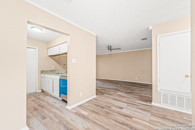 kitchen featuring sink, white cabinetry, a textured ceiling, light wood-type flooring, and ornamental molding