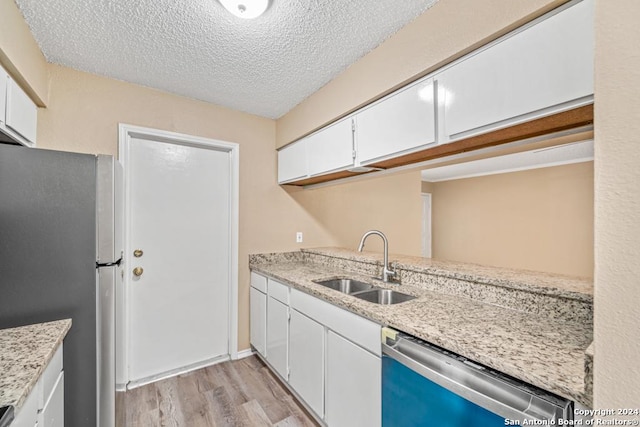 kitchen with stainless steel appliances, white cabinetry, sink, and light hardwood / wood-style floors