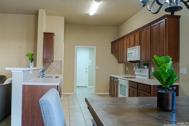 kitchen featuring sink, white appliances, light tile patterned floors, decorative backsplash, and kitchen peninsula