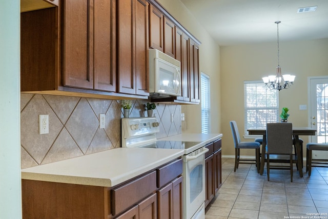 kitchen featuring light tile patterned flooring, decorative backsplash, hanging light fixtures, white appliances, and an inviting chandelier