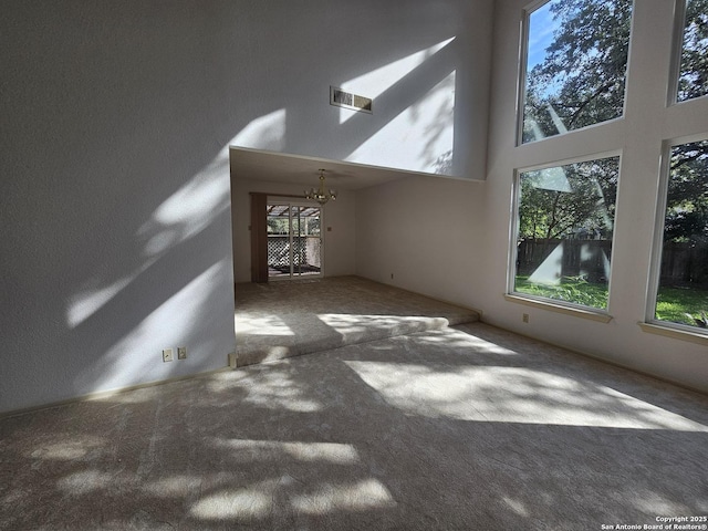 unfurnished living room with carpet flooring, a high ceiling, and a notable chandelier