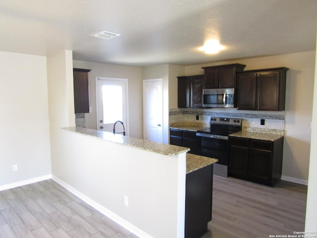 kitchen featuring sink, light stone counters, kitchen peninsula, stainless steel appliances, and backsplash