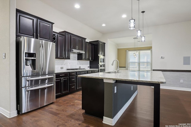 kitchen featuring appliances with stainless steel finishes, decorative light fixtures, a kitchen bar, a kitchen island with sink, and light stone counters