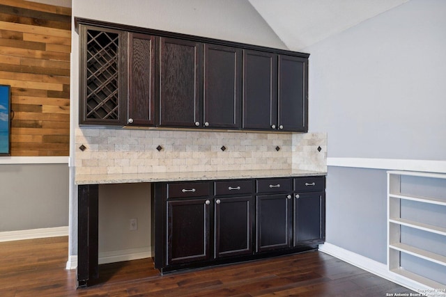 bar with dark hardwood / wood-style floors, lofted ceiling, decorative backsplash, dark brown cabinetry, and light stone countertops