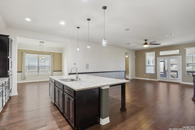 kitchen featuring appliances with stainless steel finishes, decorative light fixtures, sink, light stone countertops, and a center island with sink