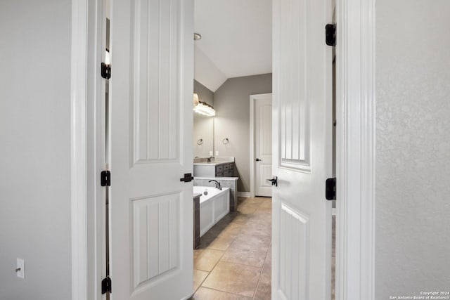 bathroom featuring vanity, a bathtub, vaulted ceiling, and tile patterned floors