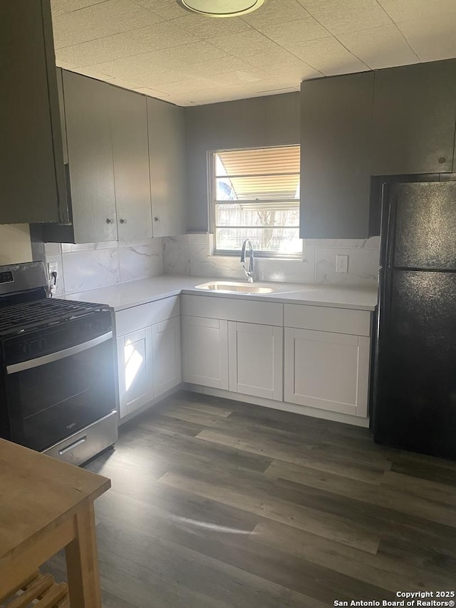 kitchen featuring black refrigerator, sink, white cabinetry, and stainless steel gas range oven