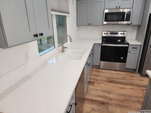 kitchen with gray cabinets, appliances with stainless steel finishes, sink, decorative backsplash, and light hardwood / wood-style floors