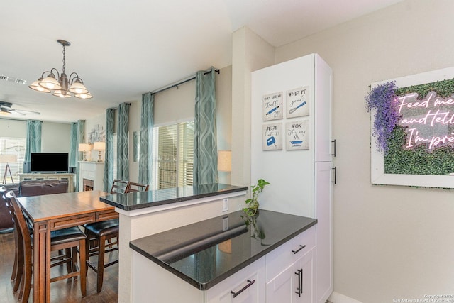 kitchen featuring ceiling fan with notable chandelier, kitchen peninsula, white cabinets, and decorative light fixtures