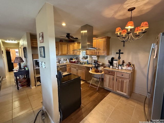 kitchen featuring hanging light fixtures, stainless steel refrigerator, island exhaust hood, light stone countertops, and ceiling fan with notable chandelier