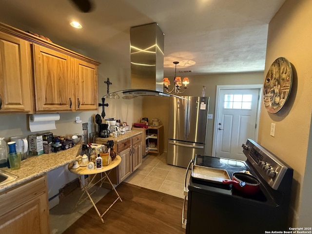 kitchen featuring appliances with stainless steel finishes, island range hood, a notable chandelier, light stone counters, and light wood-type flooring