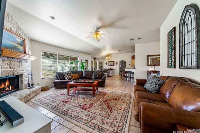 tiled living room with lofted ceiling, ceiling fan, a stone fireplace, and a textured ceiling