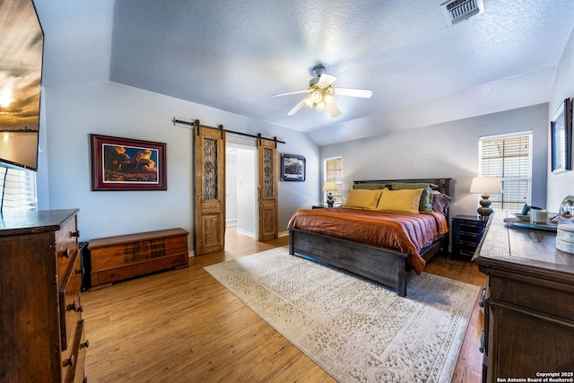 bedroom featuring lofted ceiling, a textured ceiling, hardwood / wood-style flooring, ceiling fan, and a barn door