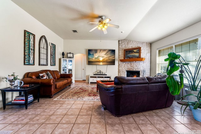 living room with light tile patterned floors, a stone fireplace, vaulted ceiling, and ceiling fan