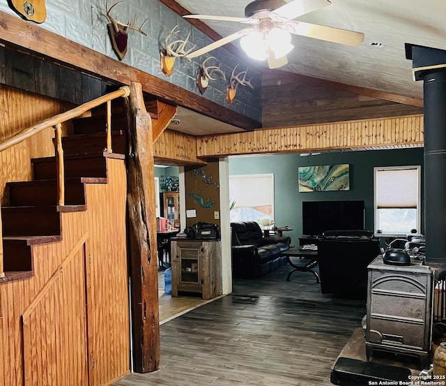 interior space featuring wood-type flooring, vaulted ceiling, a wood stove, wooden walls, and ceiling fan