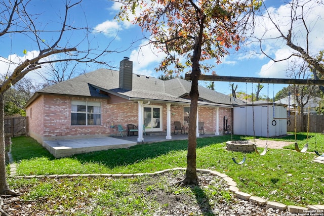 back of house featuring a storage shed, a fire pit, a patio area, and a lawn