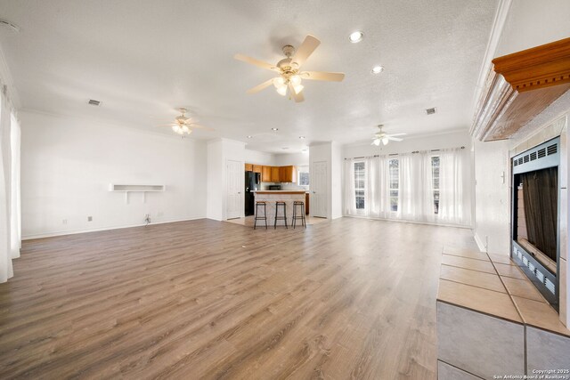 unfurnished living room with a tile fireplace, light wood-type flooring, ceiling fan, crown molding, and a textured ceiling