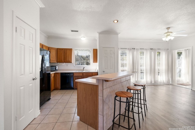 kitchen featuring sink, a center island, black appliances, a textured ceiling, and a kitchen bar