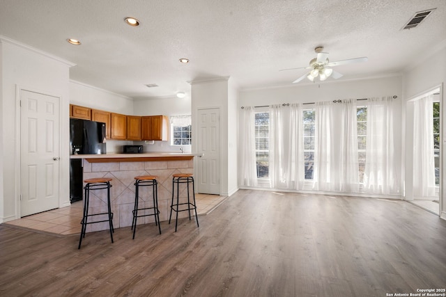 kitchen featuring black refrigerator, a breakfast bar, a healthy amount of sunlight, and light wood-type flooring