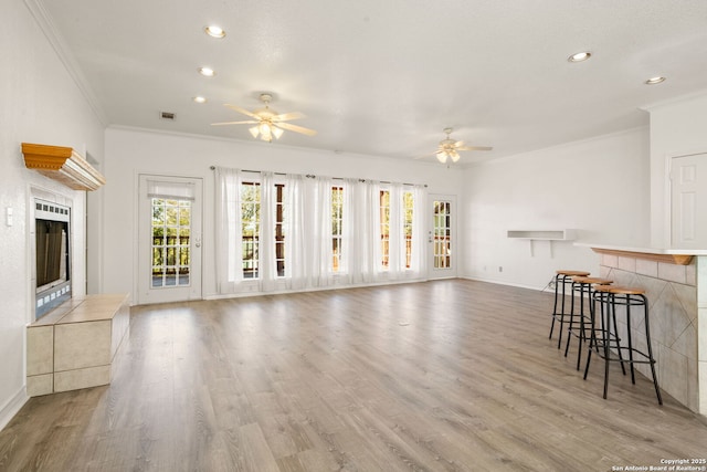 unfurnished living room featuring a tiled fireplace, crown molding, light hardwood / wood-style flooring, and ceiling fan