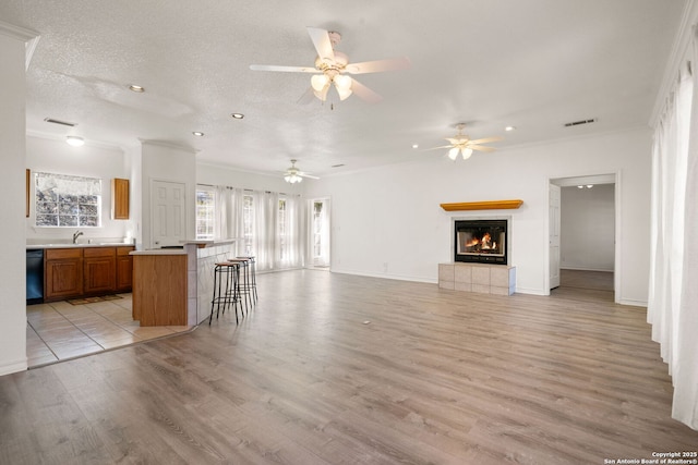 unfurnished living room featuring sink, light hardwood / wood-style flooring, ornamental molding, a textured ceiling, and a tiled fireplace