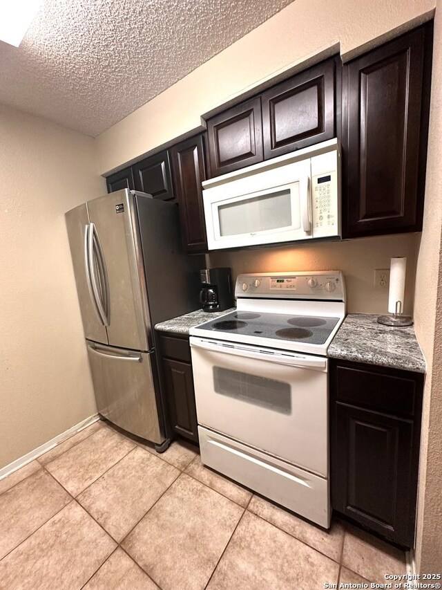 kitchen featuring dark brown cabinetry, light tile patterned flooring, a textured ceiling, and white appliances