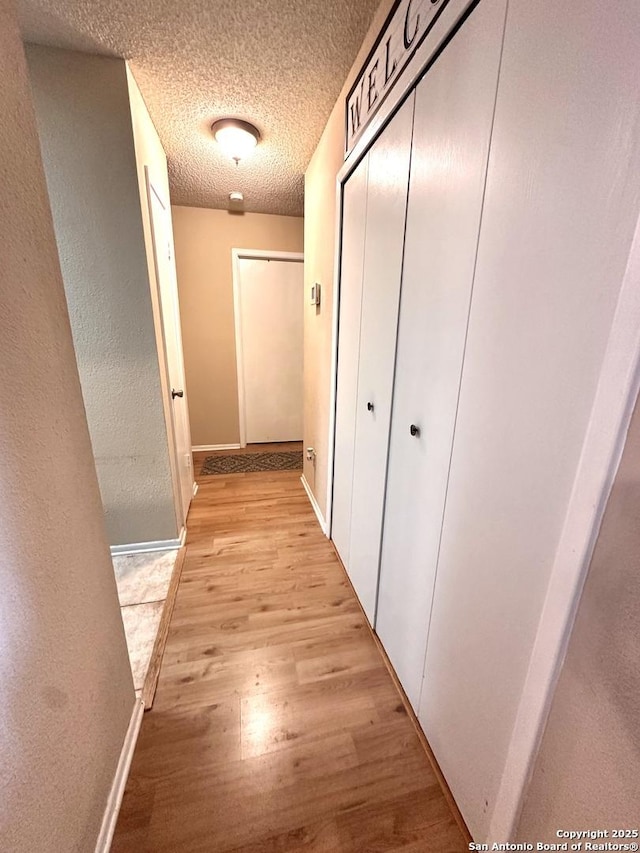 corridor with light hardwood / wood-style floors and a textured ceiling