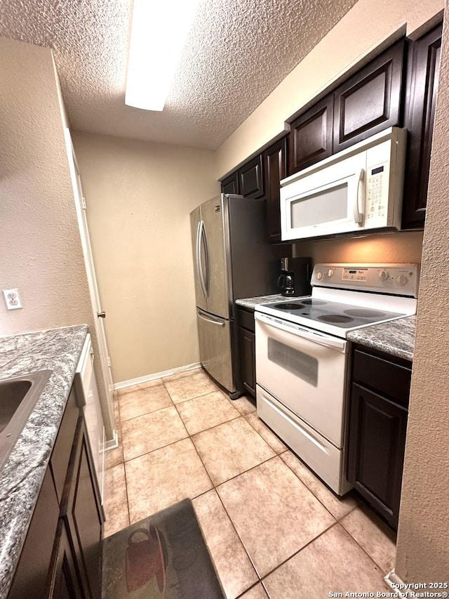 kitchen with white appliances, dark brown cabinets, a textured ceiling, and light tile patterned floors