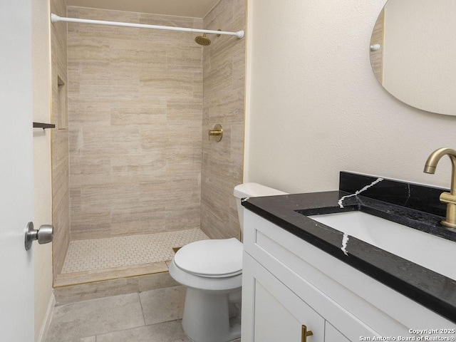 bathroom featuring vanity, tile patterned flooring, toilet, and tiled shower