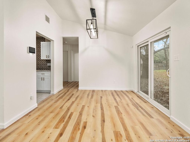 unfurnished dining area featuring vaulted ceiling and light wood-type flooring