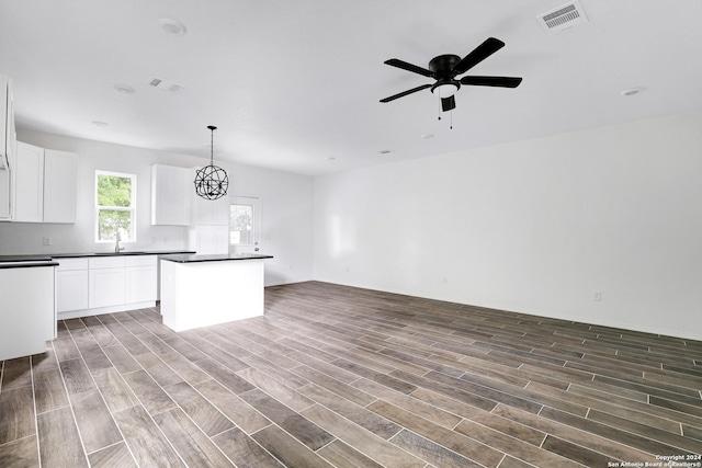 kitchen with ceiling fan with notable chandelier, white cabinetry, sink, hanging light fixtures, and a center island