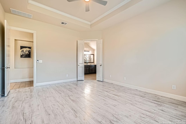 unfurnished bedroom featuring a raised ceiling, ornamental molding, ensuite bathroom, and light hardwood / wood-style flooring